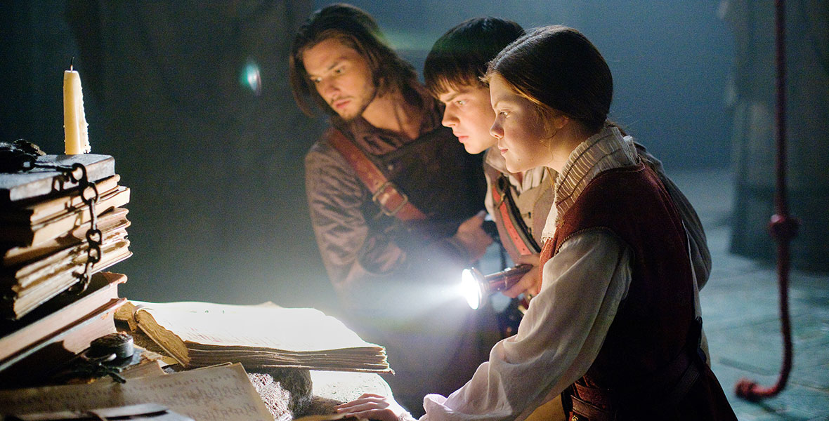 Ben Barnes, Skandar Keynes, Georgie Henley (from left to right) look at large ancient books in the film The Chronicles of Narnia: The Voyage of the Dawn Treader.