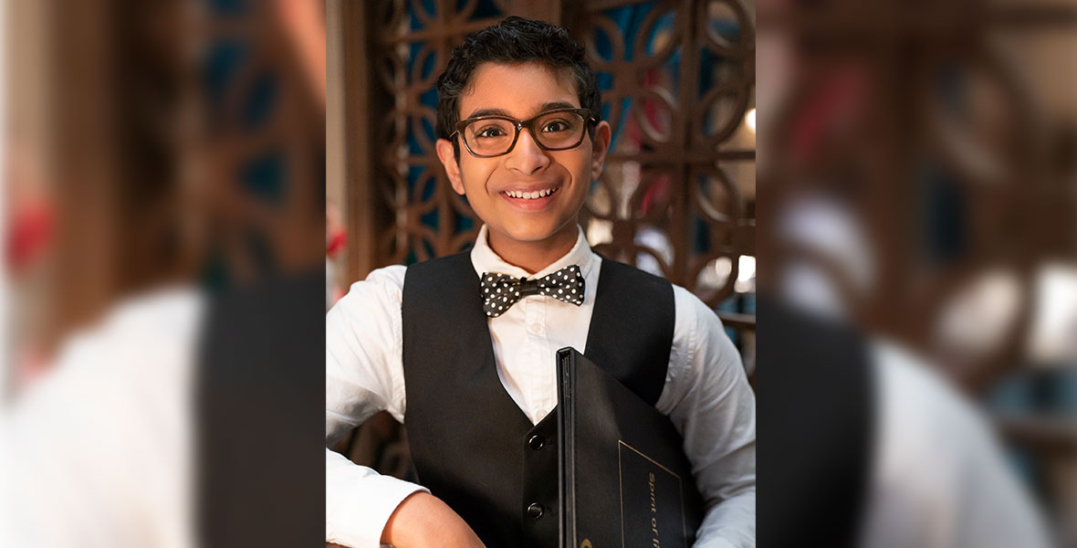 Aryan Simhadri wears.framed glasses, a bow tie and a black vest while smiling.