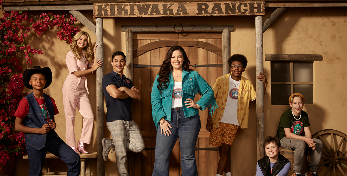 The cast of Disney Channel’s BUNK’D—Miranda May, Trevor Tordjman, Mallory James Mahoney, Israel Johnson, Shiloh Verrico, Luke Busey, and Alfred Lewis—standing in front of the rustic wooden doorway to Kikiwaka Ranch.