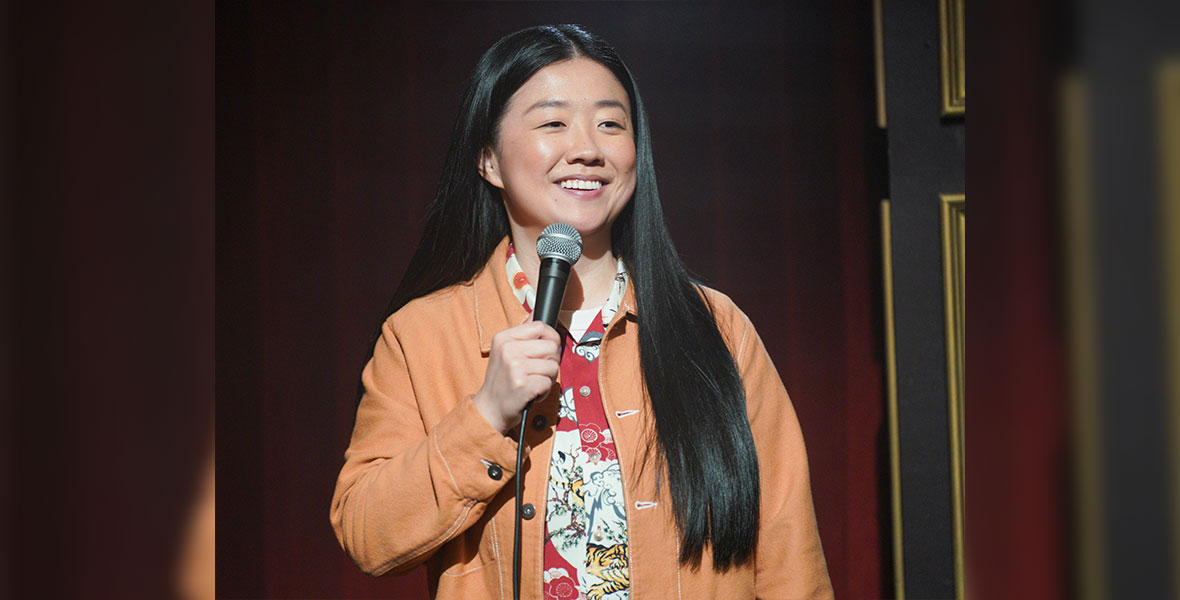 Sherry Cola performs in a tan jacket, holding a microphone.