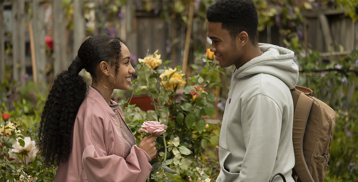 Kira King stands with El in a garden while holding a pink rose
