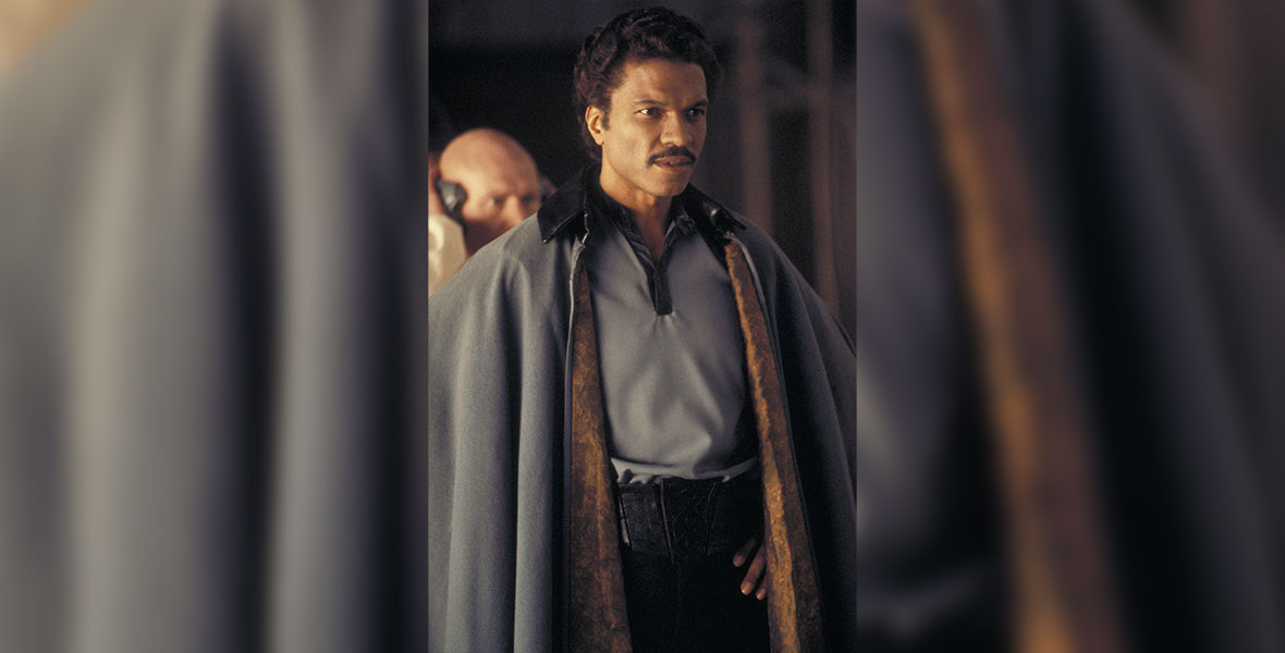 Lando Calrissian stands in a confident pose, wearing a powder blue cape with gold lining that matches his shirt.