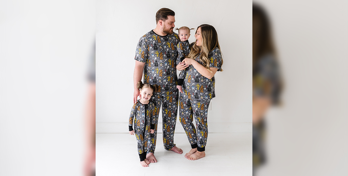 Two children and two adults pose together as a family in gray pajama sets pattered with illustrations of Darth Vader, Yoda, Chewbacca, R2-D2, and C-3PO.