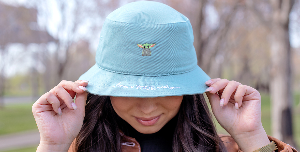 A person wearing a light blue bucket hat featuring a small embroidered illustration of Grogu (a.k.a “The Child”) from The Mandalorian.