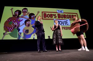 Bernard Derriman, Nora Smith, and Loren Bouchard stage onstage inside the El Capitan Theater to introduce The Bob’s Burgers Movie.