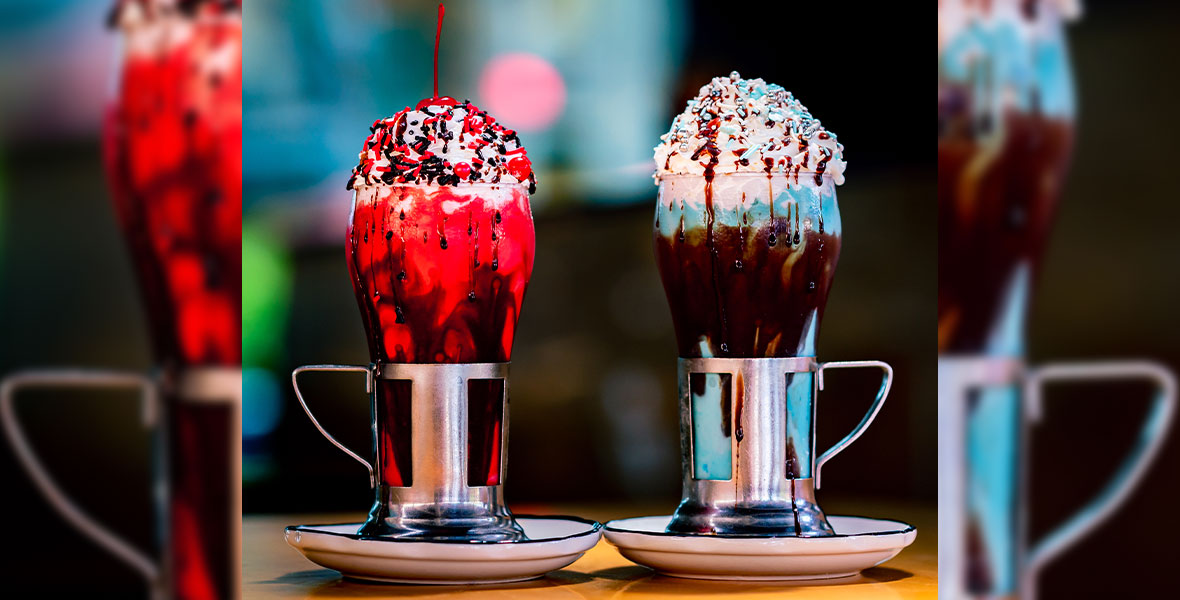 Image of both Black Tap Craft Burgers & Shakes Star Wars-themed shakes; the red Dark Classic Shake on the left, with red sprinkles and a cherry on top, and the blue Light Classic Shake on the right, with blue sprinkles. 