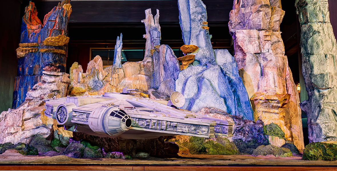 An edible showpiece depicting the Millennium Falcon arriving in Black Spire Outpost on display inside the lobby of Disney’s Grand Californian Hotel and Spay at the Disneyland Resort, with colorful rock formations in the background and the iconic Star Wars starship in the foreground.