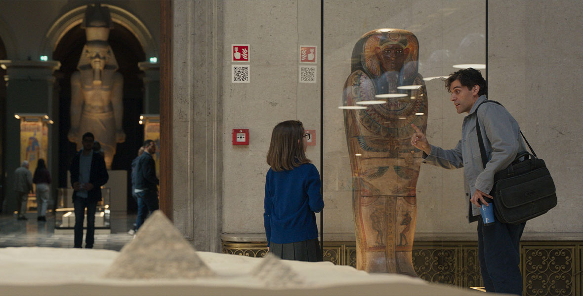 Inside an Egyptian history museum, Steven Grant discusses with a schoolgirl about the sarcophagus on display. On the wall behind them is a QR code that, when scanned, links to a free download of the first Moon Knight comic book appearance.