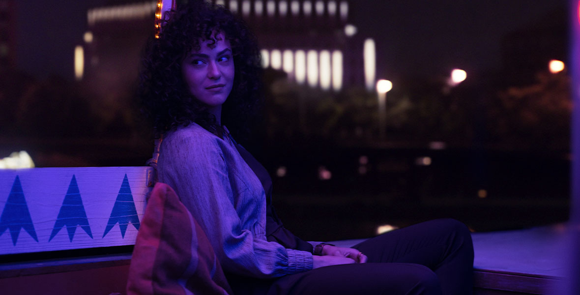 Layla sits on a boat in Egypt, bathed in purple light and looking at something out of frame.