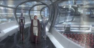 Obi-Wan Kenobi walks down the windowed hallway of the Kamoinian cloning facility. Two long-necked, thin aliens named Lama Su and Taun We walk on either side of him.