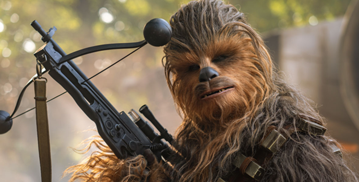 Chewbacca looks into the camera and holds up his iconic bowcaster.
