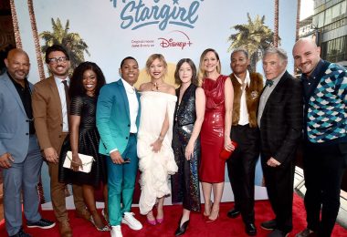 The cast and crew of Disney+’s Hollywood Stargirl pose together on the red carpet at the El Capitan Theatre in front of a large poster for the film.