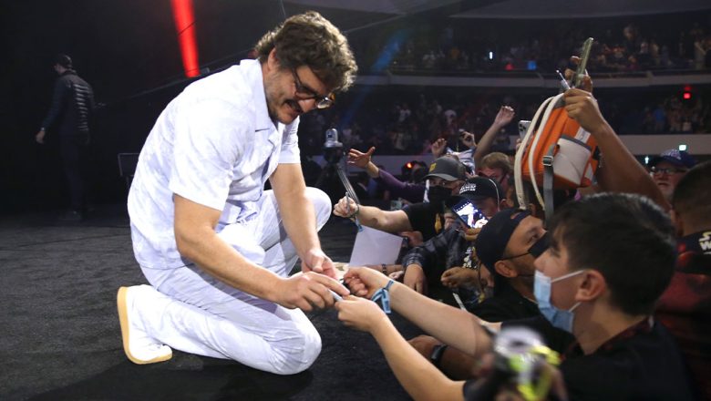 Pedro Pascal kneels on stage to sign an autograph for a fan at Star Wars Celebration