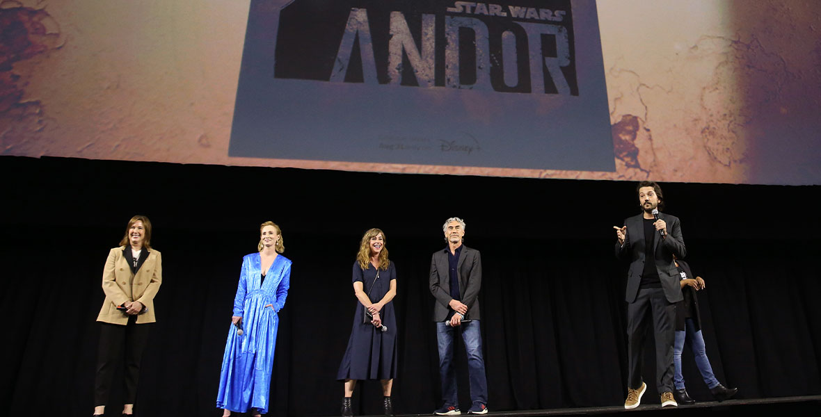 Diego Luna speaks onstage during Lucasfilm’s Studios Showcase, joined on stage by Kathleen Kennedy, Genevive O’Reilly, Sanne Wohlenberg, and Tony Gilroy. Behind them, the just-revealed Andor poster is on screen.