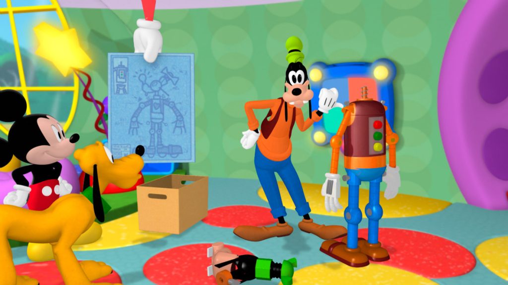 In a still from Mickey Mouse Clubhouse, Goofy stands in a room with green wallpaper, next to a robot version of himself; Mickey Mouse and Pluto are standing off to the side. A schematic of the robot is nearby.