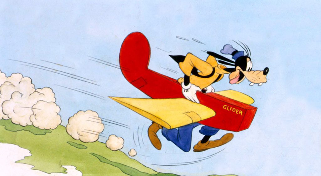 Goofy is running down a hill in a red and yellow glider, with puffs of dirt and smoke following him, in the animated short Goofy’s Glider. He’s wearing a yellow shirt and blue pants.