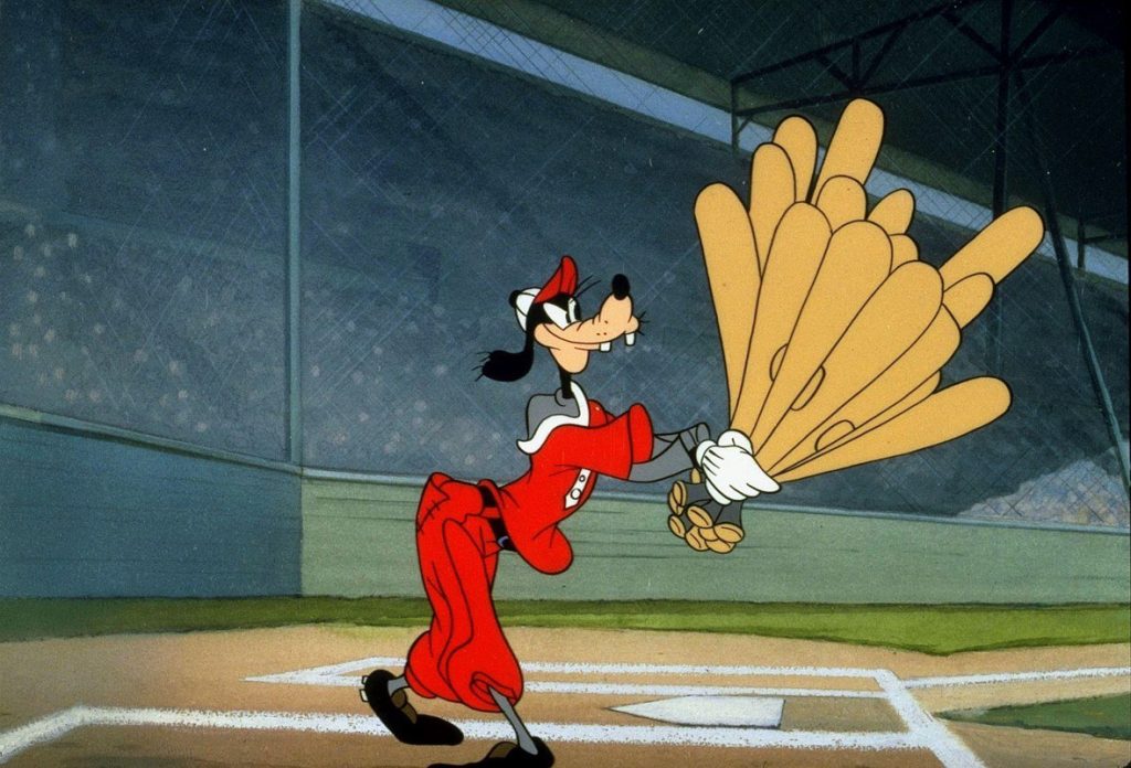 Goofy, wearing a red and white baseball uniform, holds a ridiculous number of bats as he steps up to plate in a still from the animated short How to Play Baseball.