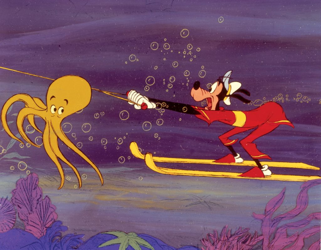 Goofy is wearing a red and yellow swimming costume as he’s water-skiing—underwater—in a still from the animated short Aquamania. There’s a yellow octopus in front of him, looking back.