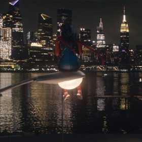 Iman Vellani as Ms. Marvel, aka Kamala Khan, sits atop a glowing streetlight as she surveys Manhattan in the distance