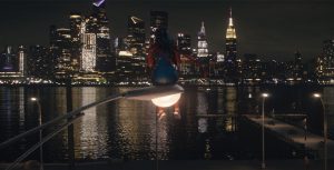 Iman Vellani as Ms. Marvel, aka Kamala Khan, sits atop a glowing streetlight as she surveys Manhattan in the distance