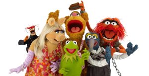 Pepé the King Prawn, Miss Piggy, Fozzie, Kermit, Gonzo, and Animal pose together against a white background. Everyone is looking at the camera except for Miss Piggy, who looks at Kermit, and Fozzie, who is reacting to Animal stealing his hat.