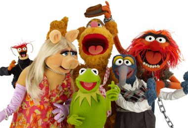 Pepé the King Prawn, Miss Piggy, Fozzie, Kermit, Gonzo, and Animal pose together against a white background. Everyone is looking at the camera except for Miss Piggy, who looks at Kermit, and Fozzie, who is reacting to Animal stealing his hat.