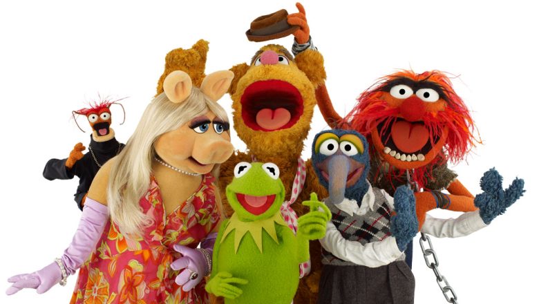Pepé the King Prawn, Miss Piggy, Fozzie, Kermit, Gonzo, and Animal pose together against a white background. Everyone is looking at the camera except for Miss Piggy, who looks at Kermit, and Fozzie, who is reacting to Animal stealing his hat.