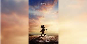 The teaser poster for Disney’s live-action Pinocchio features a silhouette of the puppet walking along a stone path—set against a pink and blue sky filled with wispy clouds, with some hills in the background.