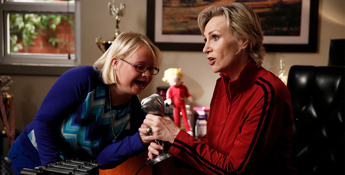 (Left to right) Becky Jackson (Lauren Potter) and Sue Sylvester (Jane Lynch) make a public address announcement to McKinley High School from the principal’s office during an episode of Glee.