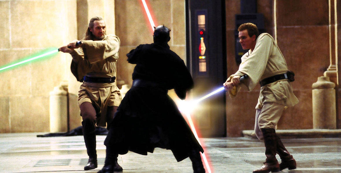 Jedis Qui-Gon Jinn (Liam Neeson), dressed in tan garb with his green lightsaber, and Obi-Wan Kenobi (Ewan McGregor), also dressed in tan with his blue lightsaber, are battling battle with Darth Maul (Ray Park)—dressed in ominous black robes wielding his red lightsaber, in a still from Star Wars: The Phantom Menace.