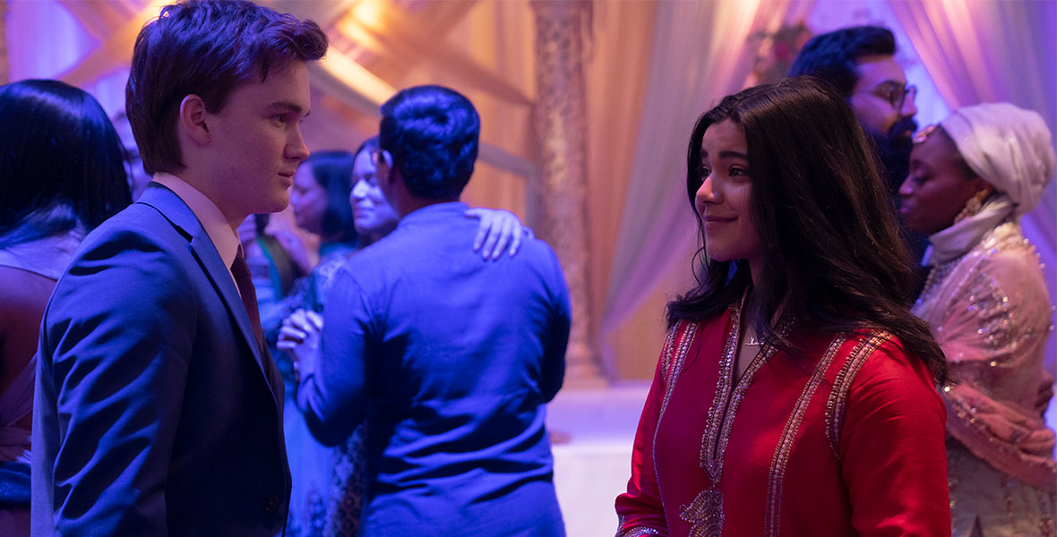 Matt Lintz as Bruno, and Iman Vellani as Kamala Khan, attend a festive event in a scene from Ms. Marvel. She wears traditional South Asian dress, and he dons a suit and tie.