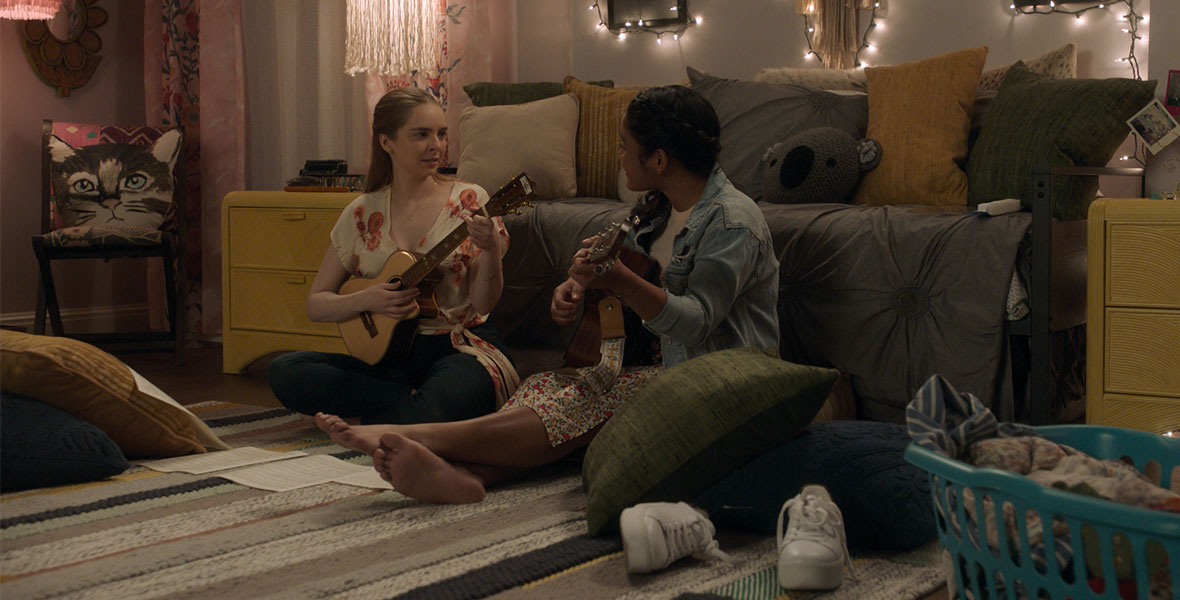 Actresses Darcy Rose Byrnes and Tisha Custodio from the Disney+ Original series Big Shot play guitar and sing while sitting on the floor in a colorful bedroom.