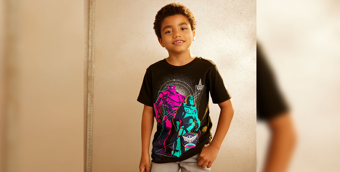 A young boy poses in a black T-shirt featuring stylized purple and blue artwork of Zurg, Buzz Lightyear, and the Star Command insignia.