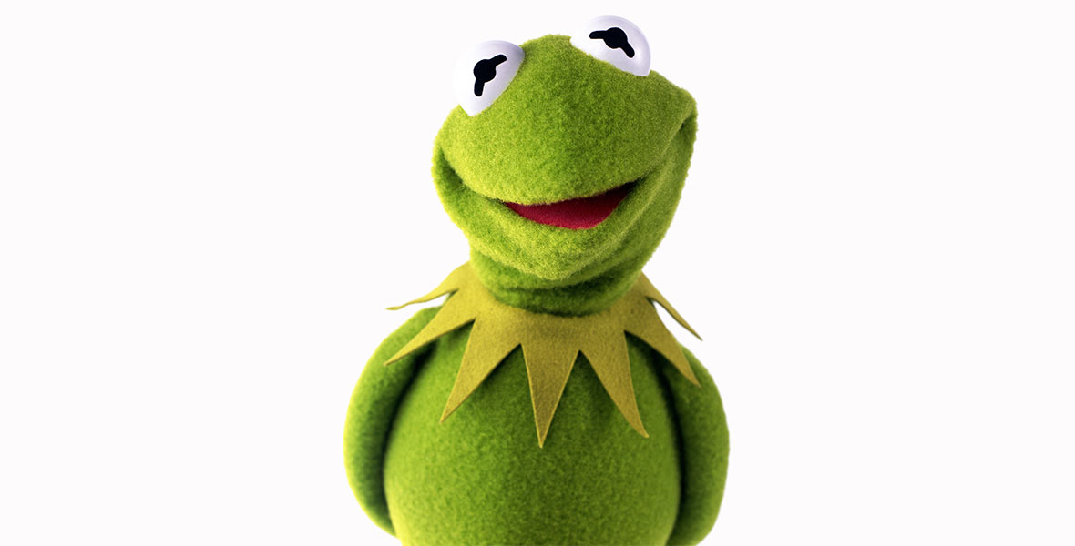 Kermit the Frog stands with hands behind his back in a headshot-style photo with a white background.