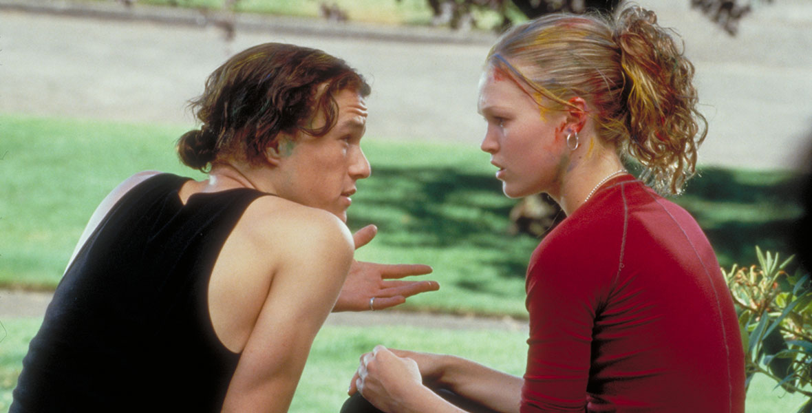 (Left to right) Patrick Verona (Heath Ledger) and Kat Stratford (Julia Stiles) sit on a curb outside facing each other in the movie 10 Things I Hate About You.