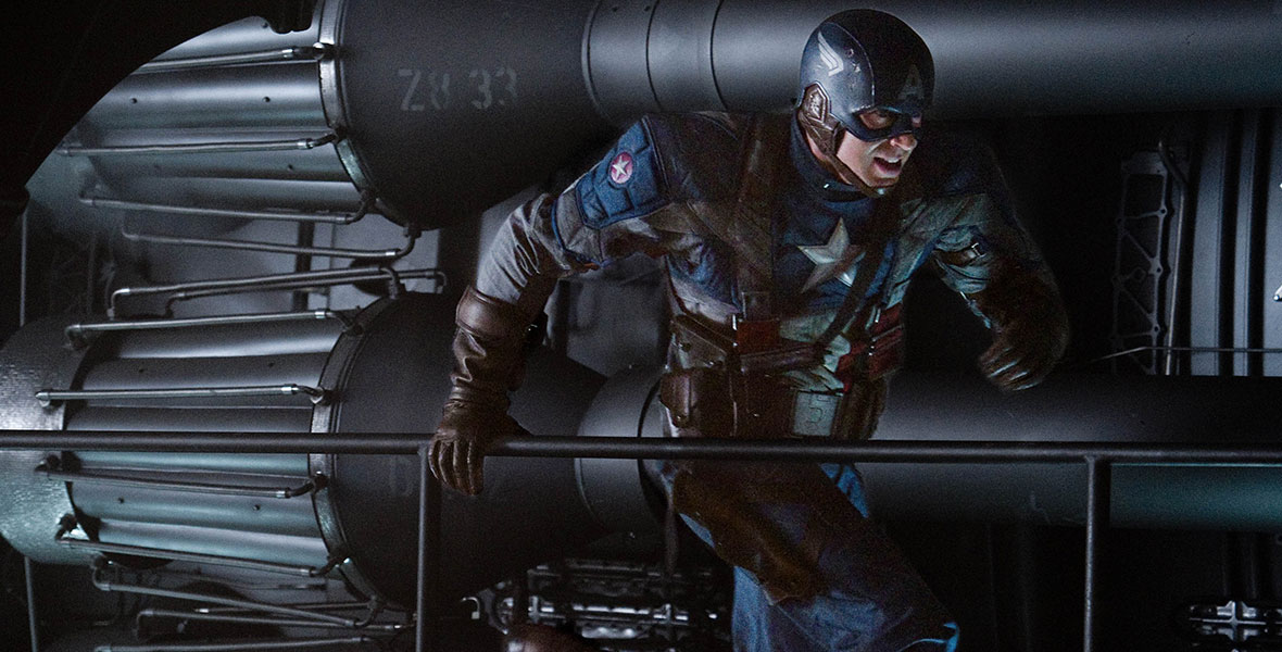Outfitted as Steve Rogers aka Captain America in his star-spangled military uniform, which includes brown gloves, brown boots, and a winged helmet, Chris Evans runs through a ship.