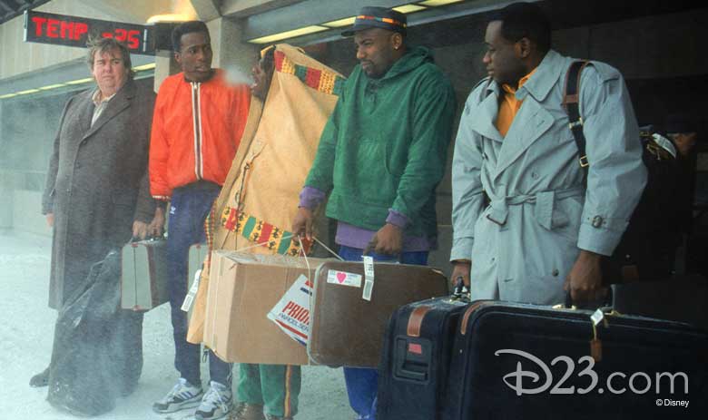 Beloved comedian John Candy stands with four actors playing members of the Jamaica national bobsled team in a snowy scene. The bobsled members look miserable and cold.