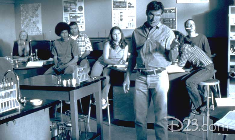 Dennis Quaid as Jim Morris, stands in the middle of his high school classroom mid-instruction as several students look on.
