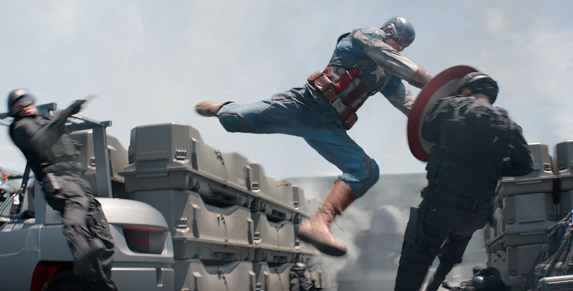 In Captain America: The Winter Soldier, Chris Evans’ Captain America, wearing his red, white, and blue uniform, uses his shield to pummel a HYDRA operative. He has kicked another enemy away.