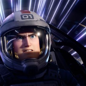 Still of Buzz Lightyear in the cockpit of a spaceship from Disney and Pixar’s Lightyear. He is wearing a helmet, and there are blue, purple, and white streaks of light seen behind him.
