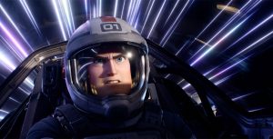 Still of Buzz Lightyear in the cockpit of a spaceship from Disney and Pixar’s Lightyear. He is wearing a helmet, and there are blue, purple, and white streaks of light seen behind him.