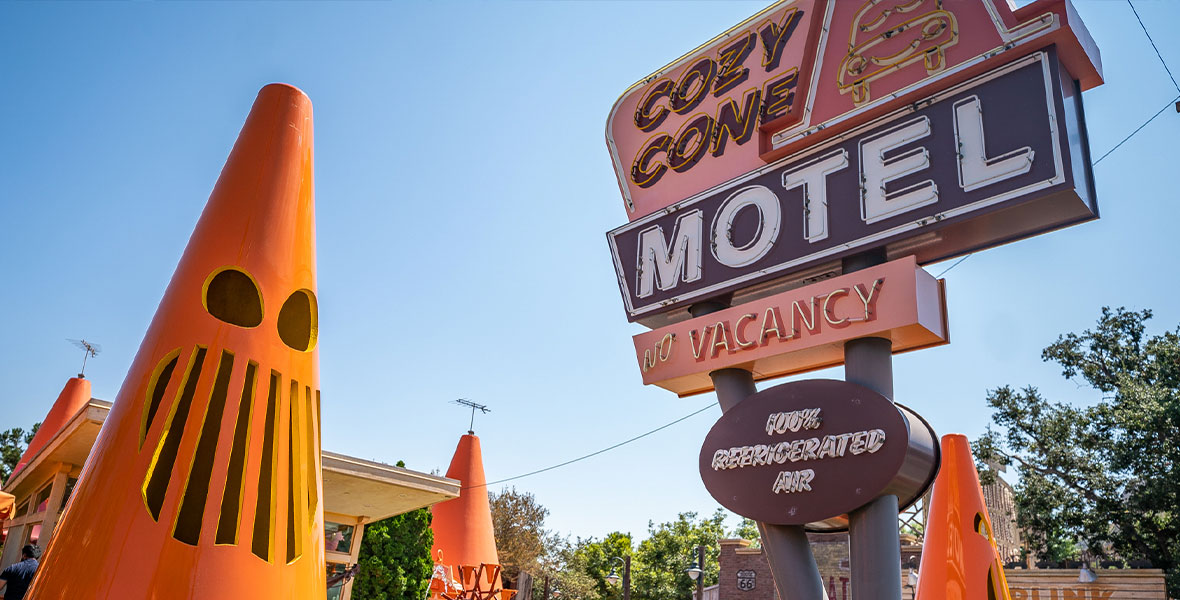 A photograph of Cars Land during the day with its Radiator Screams Halloween overlay. The Cozy Cone oversized orange traffic cones feature spooky Jack-O-Lantern carvings.