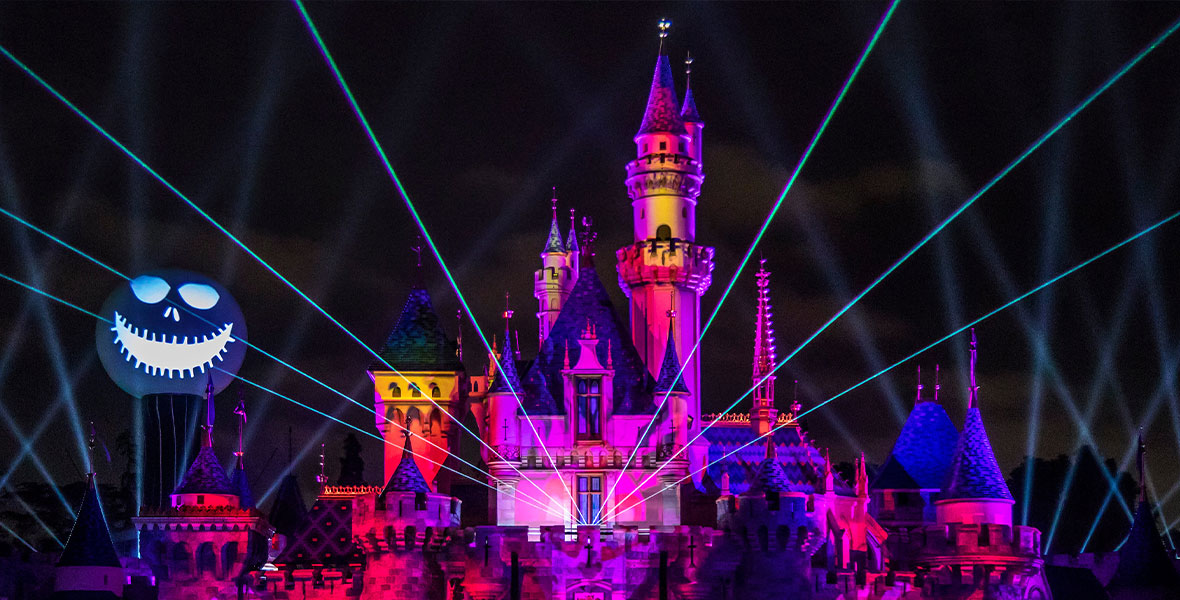 Sleeping Beauty Castle during Halloween Screams. Jack Skellington’s head looms to the left while lasers shoot out towards the crowd and spooky skeleton projections cover the castle.