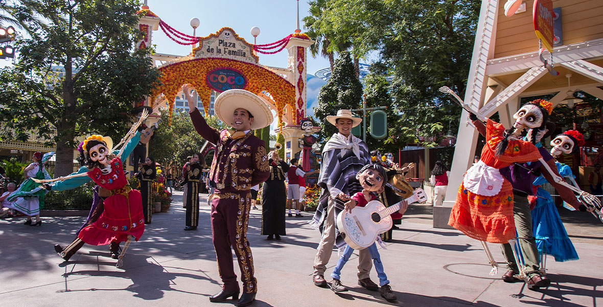 Performers from “A Musical Celebration of Coco” dance and sing in front of Plaza de la Familia at Paradise Gardens. Skeleton dancers, singers, and a puppeteer animating Miguel can be seen.