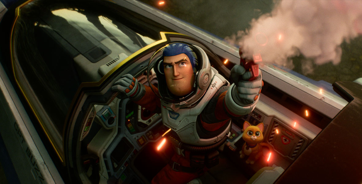 In a still from Disney and Pixar’s Lightyear, Buzz, wearing a spacesuit, stands in the open cockpit of a spaceship and shoots a flare into the sky; there is smoke and light coming from the flare gun. Sox, his robot companion, is to his right.