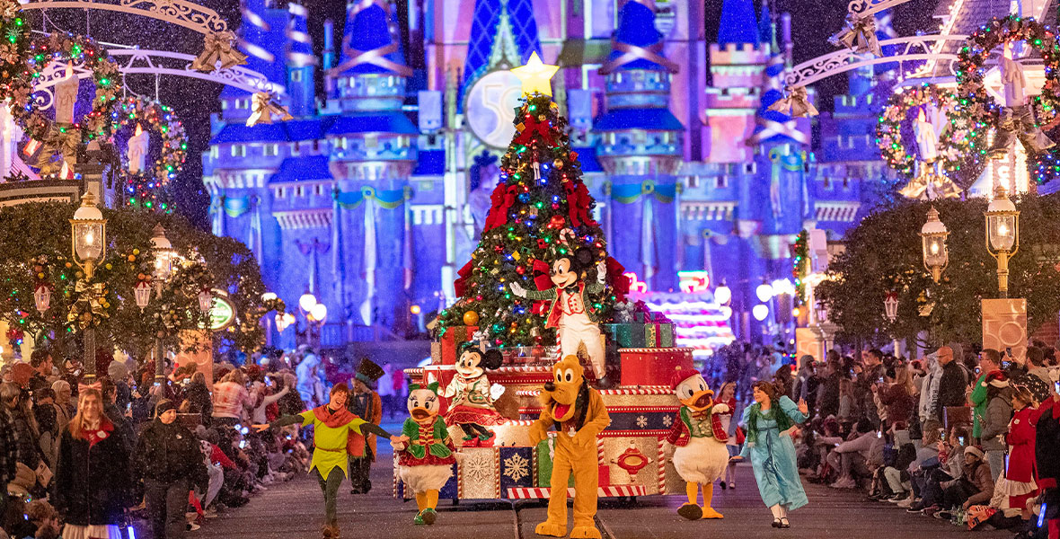 Wearing festive red and green holiday attire, Mickey Mouse, Peter Pan, Daisy Duck, Minnie Mouse, Pluto, Donald Duck, and Wendy wave at guests on Main Street, U.S.A., at Magic Kingdom at Walt Disney World Resort. Mickey is standing on the parade float in front of a trimmed Christmas tree, featuring twinkling rainbow lights, red bows, and a giant yellow star, while his friends make their way through the street. In the background, Cinderella Castle is illuminated in EARidescent colors as part of the Walt Disney World Resort’s 50th Anniversary Celebration.