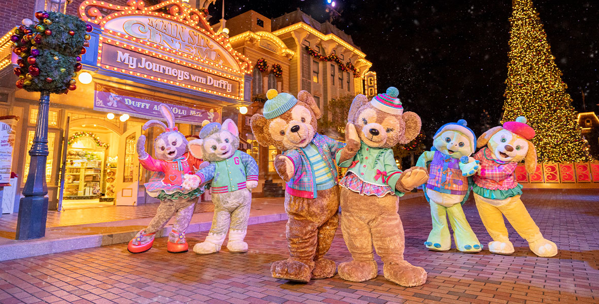 Duffy and friends pose outside of the Main Street Cinema, wearing pastel green and pink outfits. The streets are decorated with Christmas lights, and in the background, the Christmas tree is lit up.