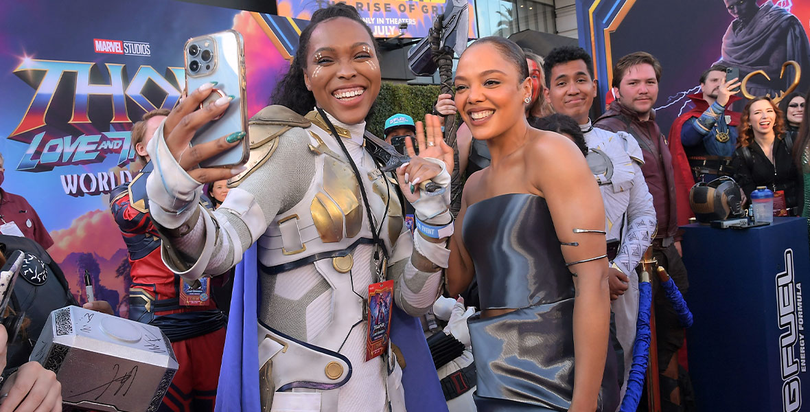 A cosplayer dressed as Valkyrie holds an iPhone in her hand and snaps a selfie with actress Tessa Thompson, who wears a strapless metallic dress at the world premiere of Marvel Studios’ Thor: Love and Thunder.