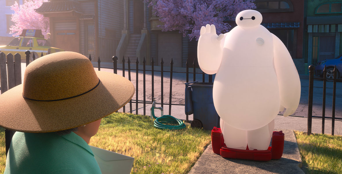 Baymax, the inflatable healthcare companion robot, stands just inside the gate of a woman’s front yard. He waves to her from the cement path; to his right is a hose, and just behind him is a trash can. A woman wearing a hat and holding an envelope faces Baymax.