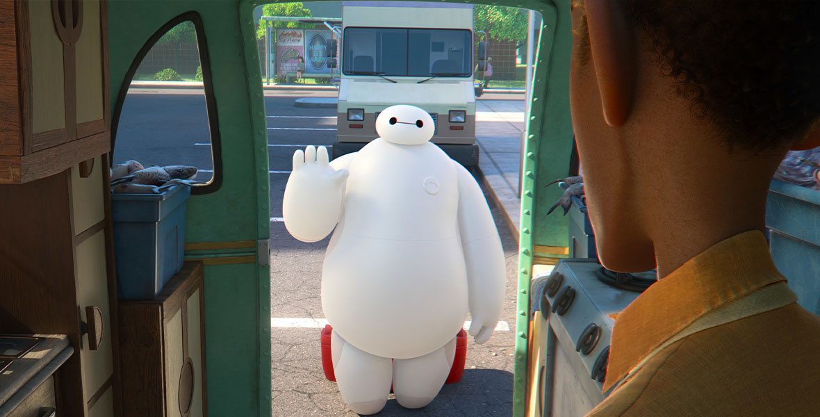 Baymax waves to a man, who is facing the inflatable healthcare companion robot while standing inside a trailer.